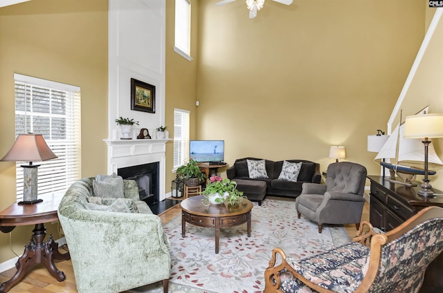 living room featuring a ceiling fan, wood finished floors, baseboards, a towering ceiling, and a large fireplace