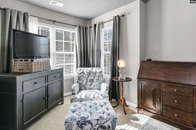 sitting room with a textured ceiling, plenty of natural light, visible vents, and light carpet