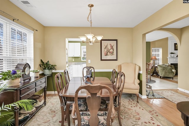 dining space with visible vents, arched walkways, a fireplace, light wood finished floors, and a chandelier