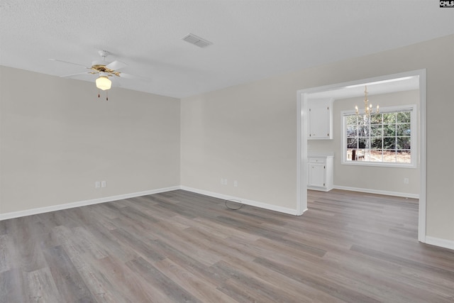 empty room with visible vents, ceiling fan with notable chandelier, a textured ceiling, wood finished floors, and baseboards