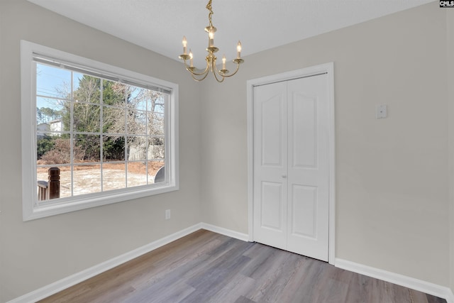 unfurnished dining area with a notable chandelier, baseboards, and wood finished floors