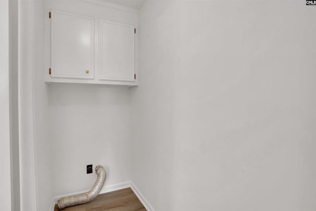 clothes washing area with cabinet space, hookup for an electric dryer, baseboards, and wood finished floors