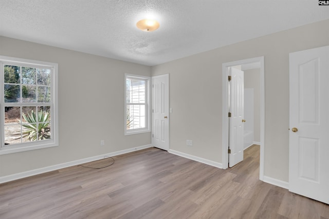 unfurnished bedroom with light wood finished floors, a textured ceiling, and baseboards