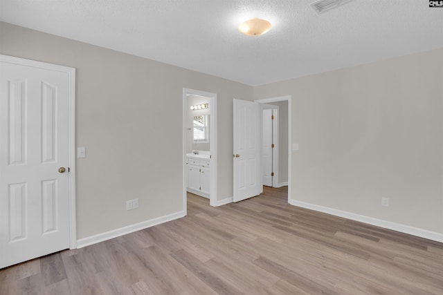 unfurnished bedroom featuring light wood finished floors, visible vents, baseboards, ensuite bath, and a textured ceiling