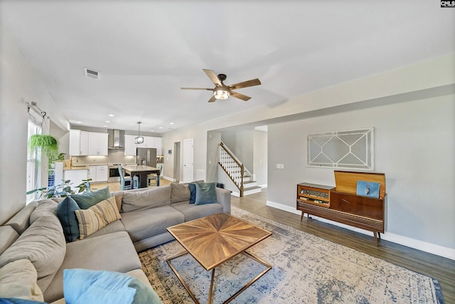 living room featuring wood finished floors, visible vents, baseboards, recessed lighting, and stairs