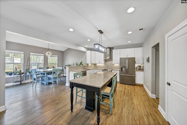 kitchen with stainless steel appliances, a peninsula, light wood-style flooring, and wall chimney range hood