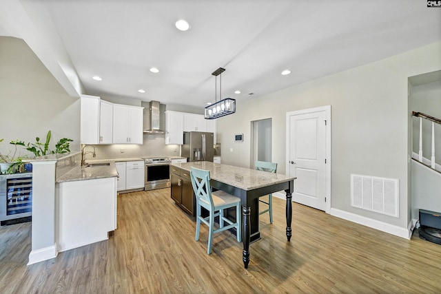 kitchen with beverage cooler, visible vents, a sink, appliances with stainless steel finishes, and wall chimney range hood