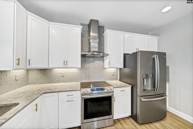 kitchen with light wood-type flooring, tasteful backsplash, white cabinetry, appliances with stainless steel finishes, and wall chimney exhaust hood