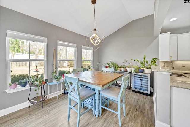 dining area featuring vaulted ceiling, light wood-style flooring, beverage cooler, and baseboards