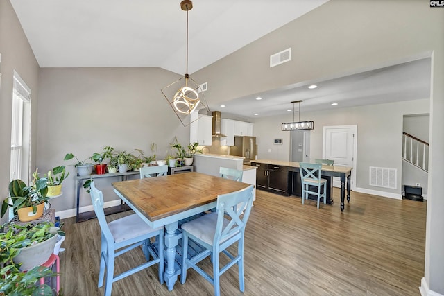 dining room featuring visible vents, light wood-style flooring, stairway, and vaulted ceiling