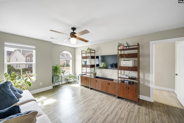 living area featuring a ceiling fan, baseboards, visible vents, and light wood finished floors