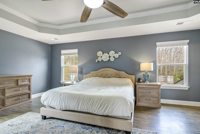 bedroom featuring ceiling fan, baseboards, ornamental molding, wood finished floors, and a raised ceiling