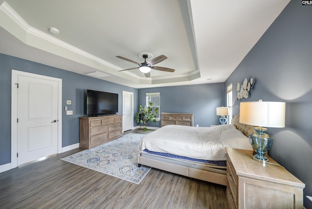 bedroom with wood finished floors, baseboards, a tray ceiling, ceiling fan, and crown molding