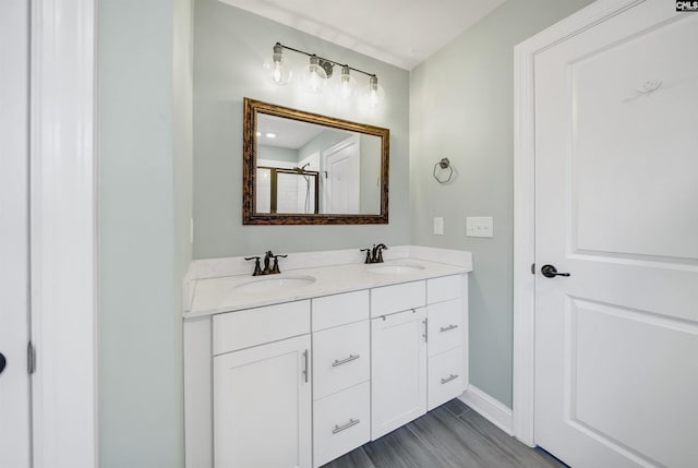 bathroom with a sink, an enclosed shower, baseboards, and double vanity