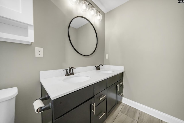 bathroom with a sink, baseboards, toilet, and double vanity