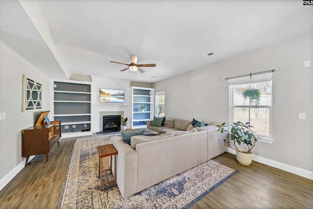 living room with a fireplace with flush hearth, a ceiling fan, baseboards, and wood finished floors