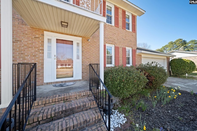 doorway to property with brick siding, an attached garage, and driveway