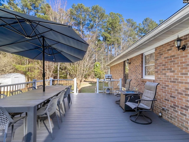 wooden deck with outdoor dining space, an outbuilding, a storage unit, and a fire pit