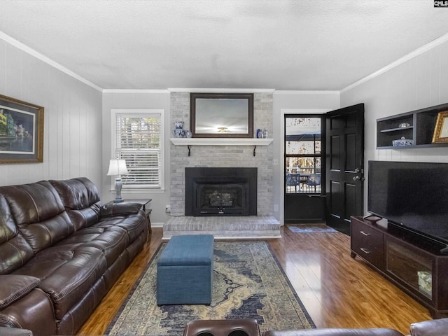 living area featuring a textured ceiling, a brick fireplace, wood finished floors, and ornamental molding