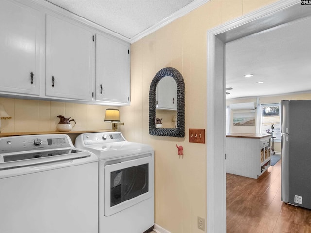 clothes washing area featuring wood finished floors, cabinet space, ornamental molding, a textured ceiling, and independent washer and dryer