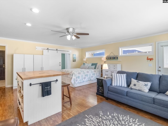 bedroom with ornamental molding, wood finished floors, recessed lighting, a barn door, and ceiling fan