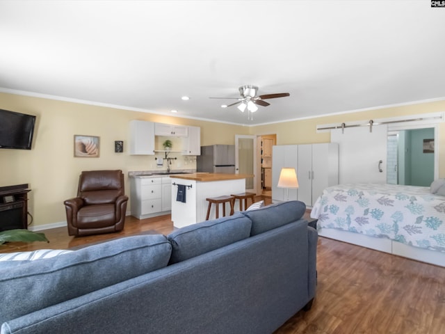 living room featuring ornamental molding, wood finished floors, a barn door, baseboards, and ceiling fan