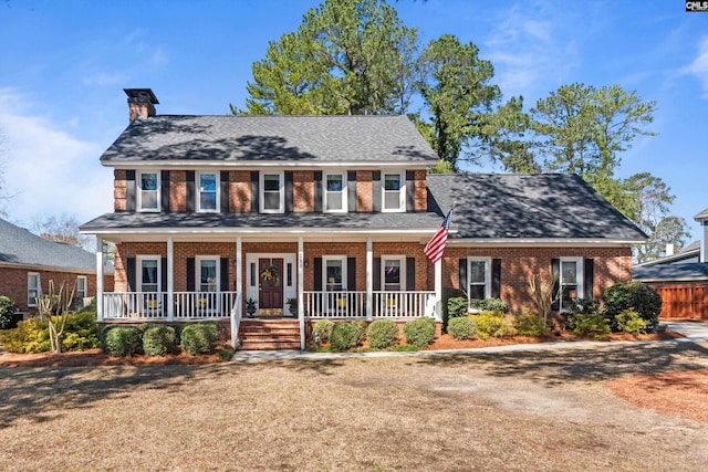 colonial home with brick siding, a porch, a chimney, and roof with shingles