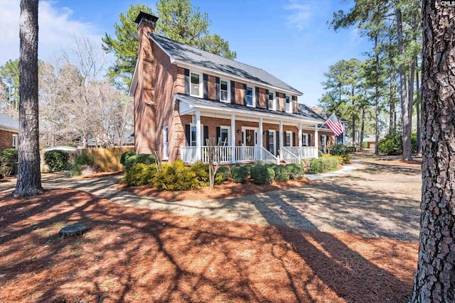 colonial home featuring brick siding, covered porch, and a chimney