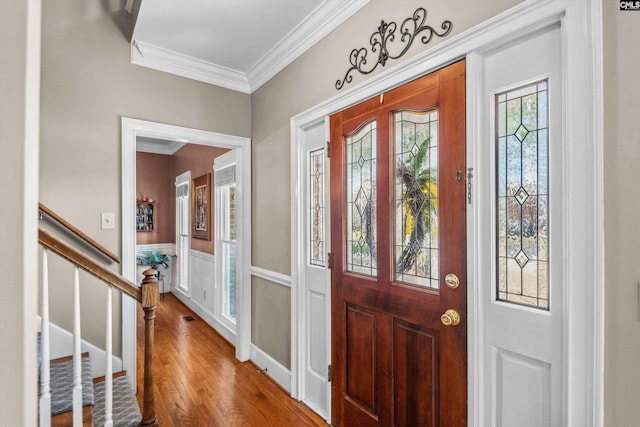 foyer entrance featuring visible vents, crown molding, stairs, wainscoting, and wood finished floors