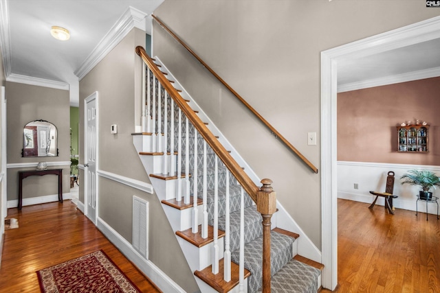 stairway with visible vents, wood finished floors, baseboards, and ornamental molding