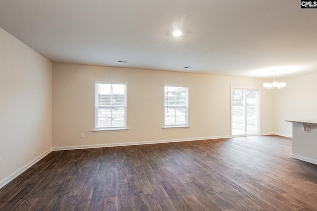 unfurnished living room with an inviting chandelier, dark wood-type flooring, and baseboards