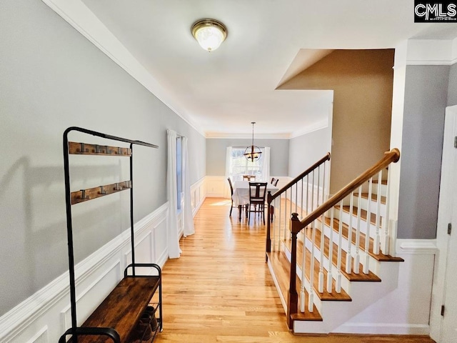 interior space with a wainscoted wall, stairway, light wood-type flooring, ornamental molding, and a decorative wall