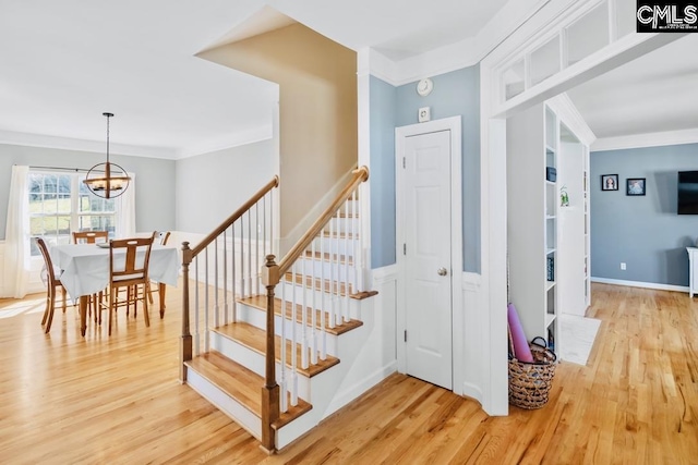 staircase with a chandelier, wood finished floors, and ornamental molding