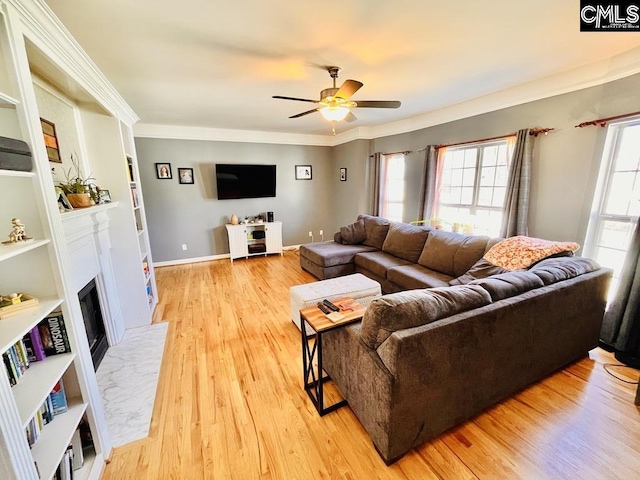 living area with a fireplace with flush hearth, a ceiling fan, crown molding, light wood finished floors, and baseboards