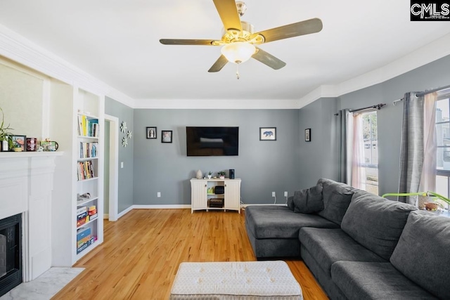 living area with baseboards, a fireplace with flush hearth, ceiling fan, and light wood finished floors