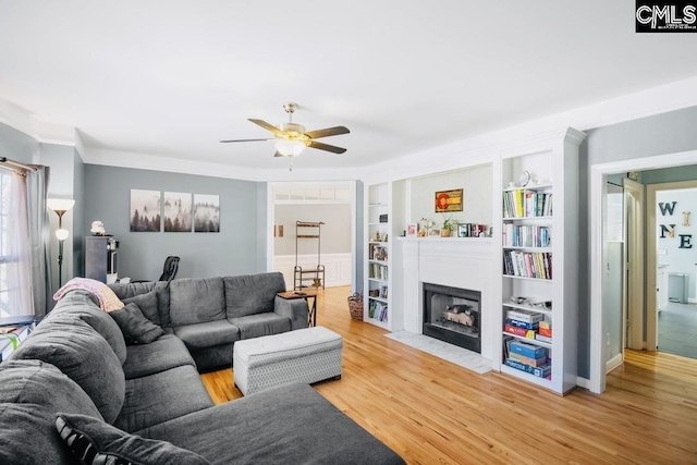 living room featuring built in shelves, a ceiling fan, a fireplace with flush hearth, and light wood finished floors