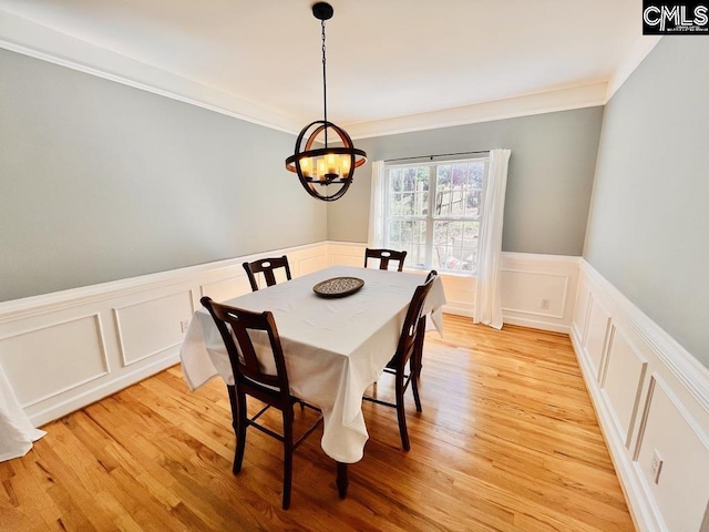 dining area with a wainscoted wall, light wood-style flooring, ornamental molding, a decorative wall, and a chandelier