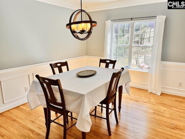 dining space with a wainscoted wall, an inviting chandelier, crown molding, and light wood finished floors