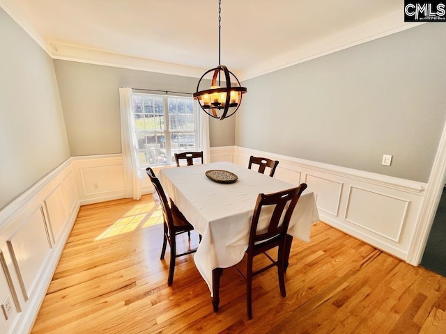 dining space with light wood-style flooring, a decorative wall, an inviting chandelier, wainscoting, and crown molding