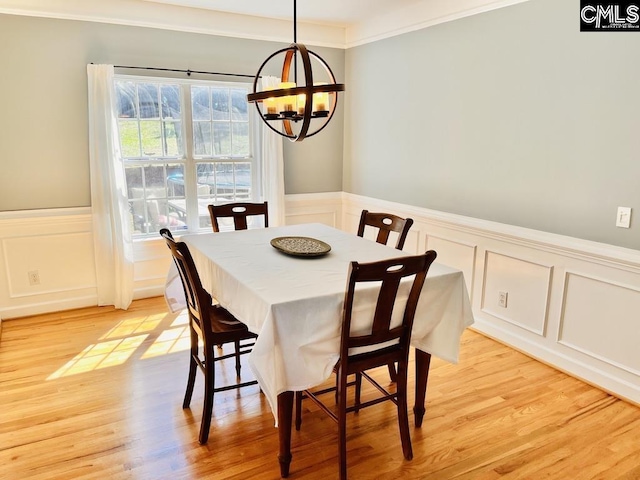 dining space featuring crown molding, a decorative wall, light wood-type flooring, and a chandelier