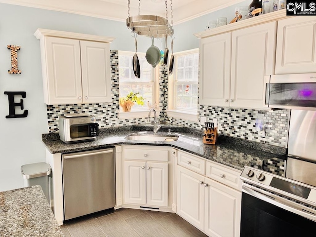 kitchen with dark stone counters, ornamental molding, decorative backsplash, a sink, and appliances with stainless steel finishes