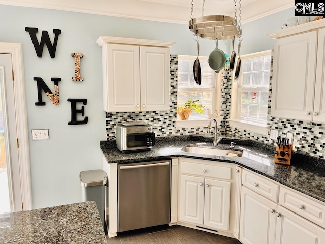 kitchen featuring dark stone countertops, a sink, stainless steel dishwasher, crown molding, and backsplash