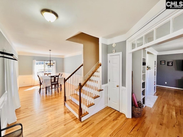 stairway featuring wainscoting, wood finished floors, crown molding, and a decorative wall