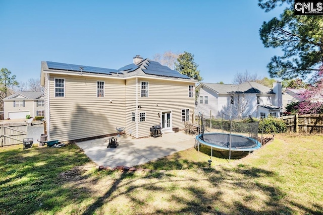 back of house with a trampoline, roof mounted solar panels, a lawn, a fenced backyard, and a patio