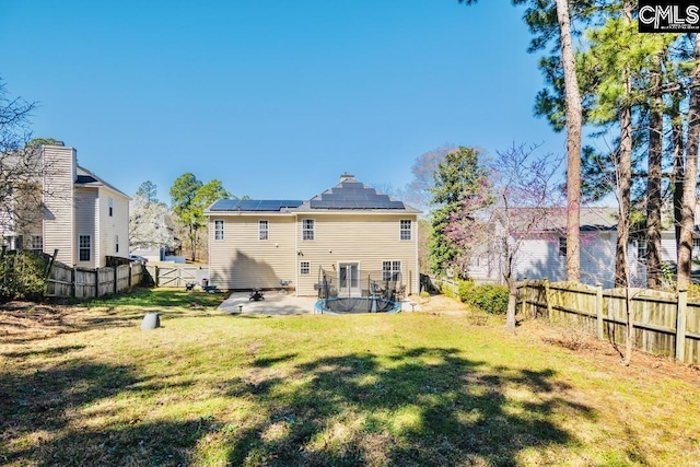 back of property with a trampoline, solar panels, a fenced backyard, and a lawn