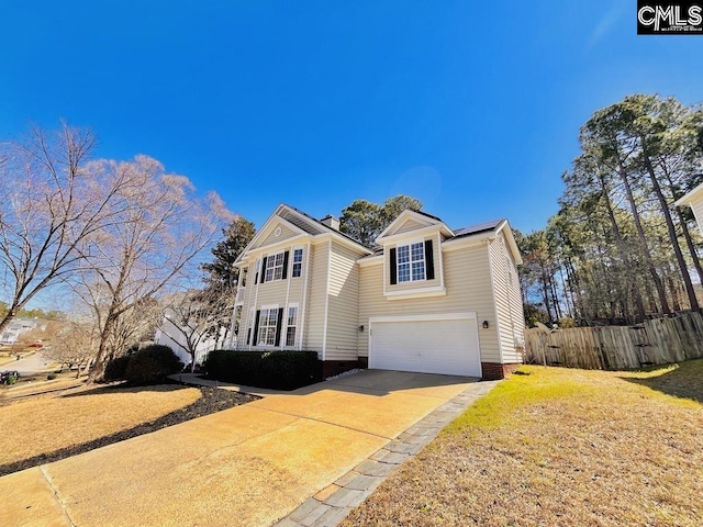 traditional-style home featuring a front yard, fence, driveway, solar panels, and an attached garage