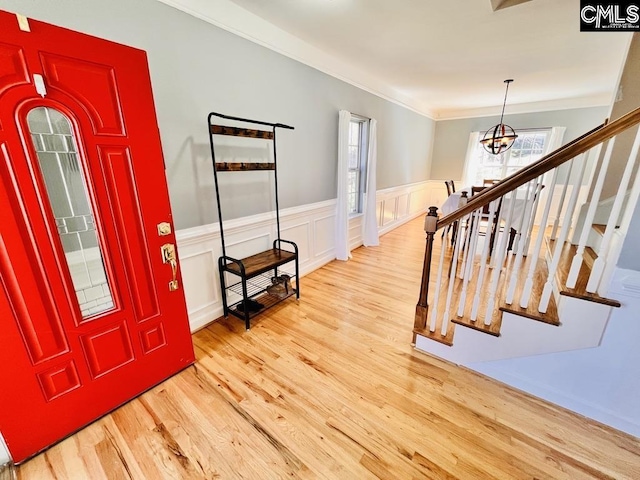 entrance foyer with an inviting chandelier, crown molding, wood finished floors, and a wainscoted wall