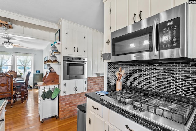 kitchen with a ceiling fan, light wood finished floors, stainless steel appliances, dark countertops, and tasteful backsplash