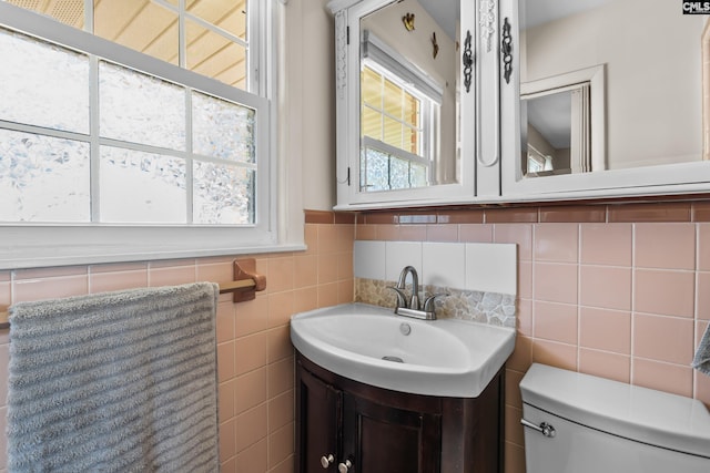 half bath with plenty of natural light, toilet, tile walls, and vanity