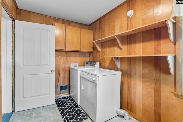 laundry area featuring washer and dryer, visible vents, cabinet space, and wooden walls